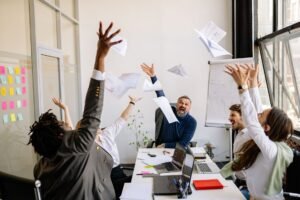 Employee Motivation Certification - A diverse office team celebrating with papers in the air, showing teamwork and success.