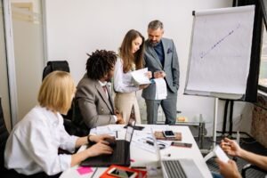 Managing a Sales Team Certification - Business professionals collaborating in a modern office meeting with charts and laptops.
