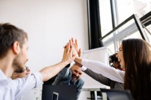 Creating and Maintaining a Successful Organisation Certification - Vibrant office team sharing a group high five in a bright workspace.