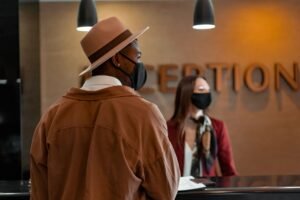 Front Desk Safety and Security Certification - Man in mask at hotel reception during pandemic, interacting with masked receptionist.