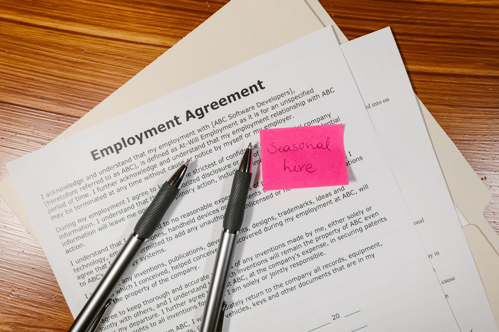 Introduction to Contracts Of Employment Certification - Top view of employment agreement contract with pens and seasonal hire note on wooden desk.