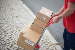 Manual Handling Certification - Courier handling packages with a cart on a cobblestone street in daylight.