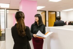 HR: Working with Vendors Certification - Two colleagues in business attire discuss documents in a bright office space.
