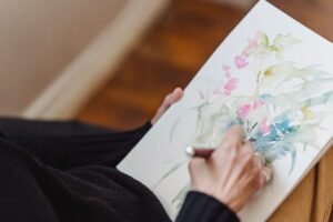 Art Therapy Certification - Close-up of hands creating a watercolor floral painting, showcasing artistic creativity.