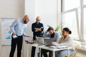 Working in Teams Certification - A diverse team discusses strategy in a modern office setting with laptops and charts.