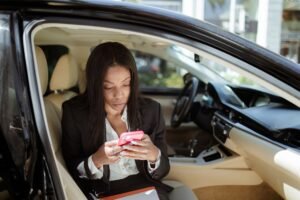 Mobile Working - A businesswoman uses her smartphone while seated in a car, focusing intently on the screen.