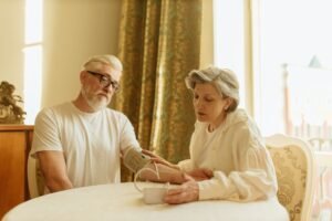 Domiciliary Care Certification - An elderly couple at home measuring blood pressure with a digital monitor, depicting care and health awareness.