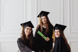 Understanding Autism Diploma - Three young women celebrating graduation with caps and diplomas indoors.