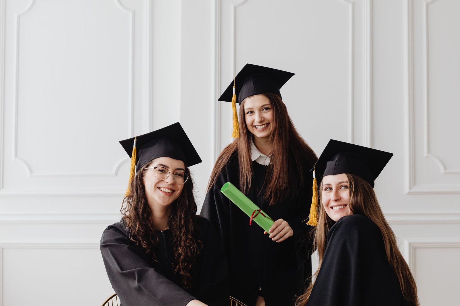 Understanding Autism Diploma - Three young women celebrating graduation with caps and diplomas indoors.