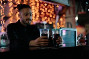Safeguarding at Events and Preventing Drink Spiking - A bartender holding cola drinks at a decorated indoor bar with festive lighting.