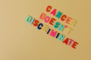 Promoting Positive Behaviour Certification - Bright letters spelling 'Cancer Doesn't Discriminate' on yellow. Advocacy message.
