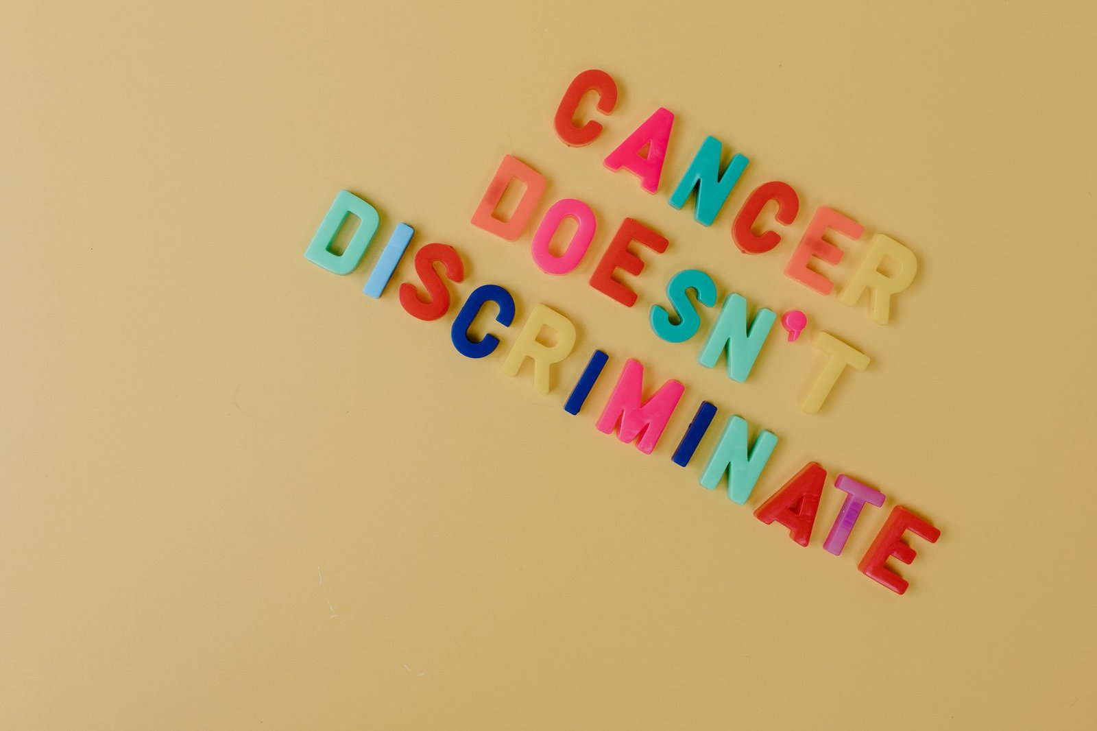 Promoting Positive Behaviour Certification - Bright letters spelling 'Cancer Doesn't Discriminate' on yellow. Advocacy message.