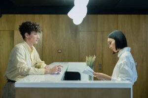 Hotel Receptionist Administration Certification - A young man and woman interacting at a modern office reception desk indoors.