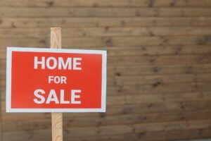 Buying and Selling Online Certification - Close-up of a red home for sale sign against a wooden backdrop, ideal for real estate use.