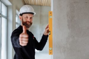 Ensuring Adequate Staff Levels Certification - Professional construction worker with hard hat and spirit level giving thumbs up indoors.