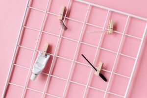 Eyelash Lift and Tint Certificate - Aesthetic flat lay of makeup essentials including mascara brush and false eyelashes on a pink backdrop with grid.