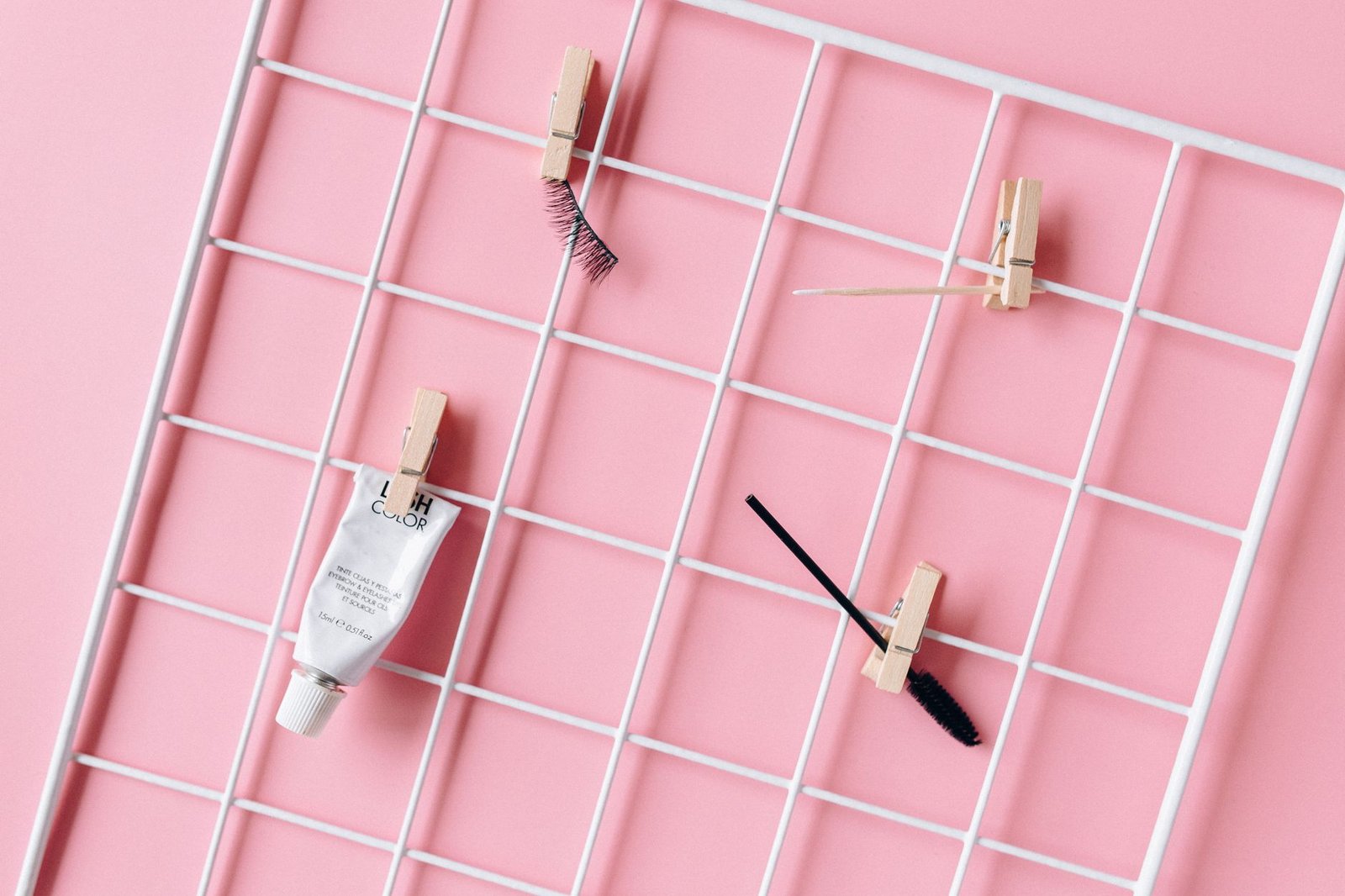 Eyelash Lift and Tint Certificate - Aesthetic flat lay of makeup essentials including mascara brush and false eyelashes on a pink backdrop with grid.