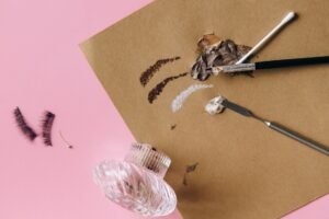 Eyelash Tinting Certificate - Flat lay of makeup tools with brushes and eyelashes on pink.