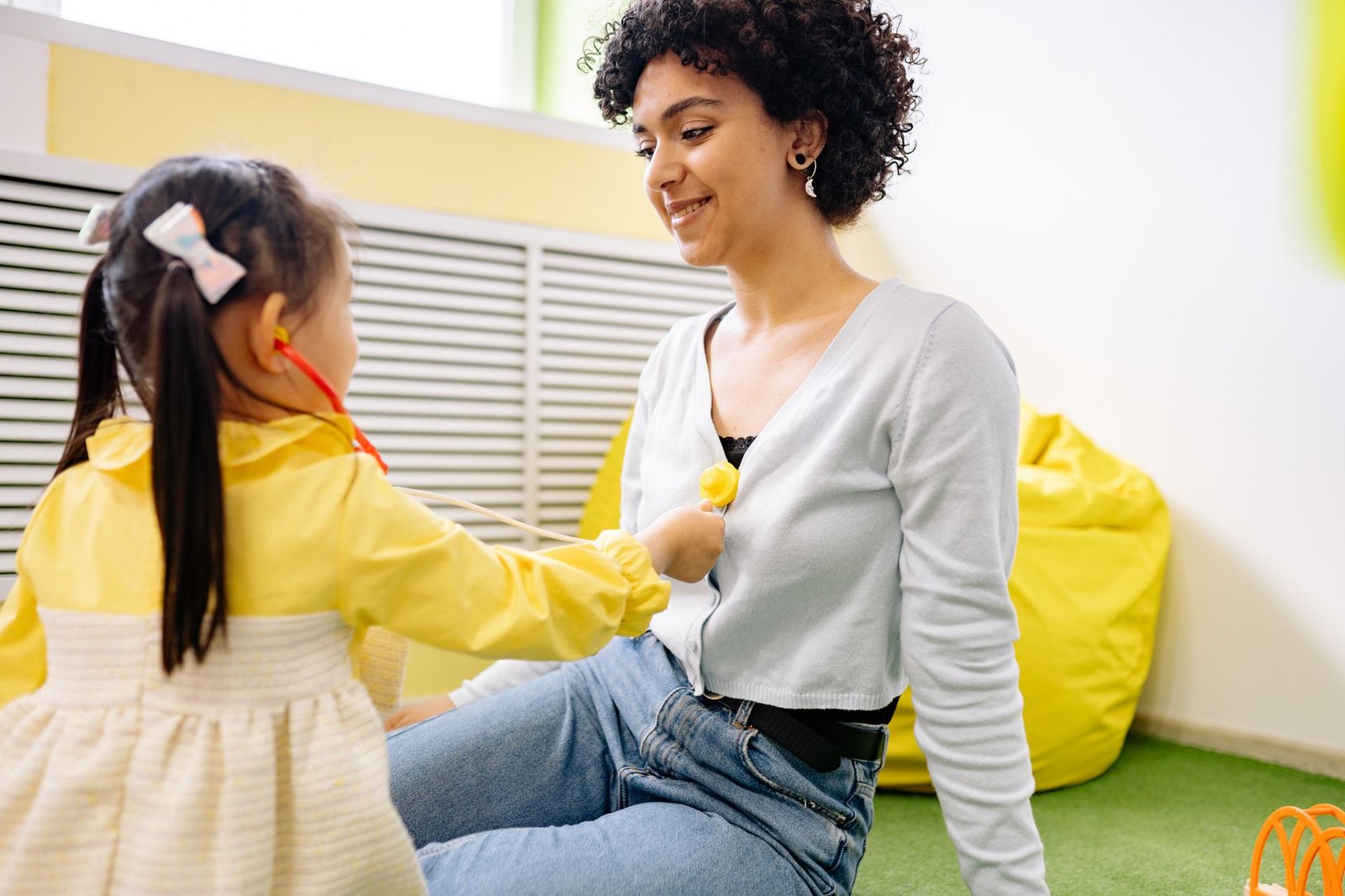Introduction to Childcare Certification - A child plays doctor with a stethoscope and a smiling adult indoors.