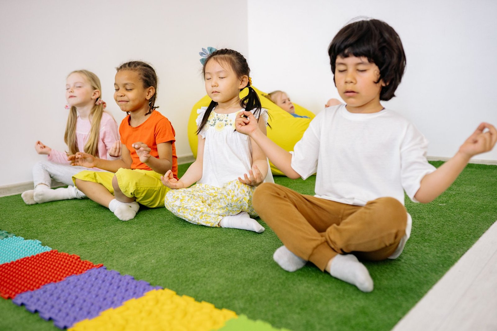 Mindfulness for Children Training Programme Certification - Group of diverse young children meditating in yoga poses on a green mat indoors.