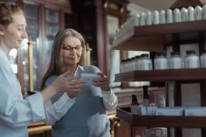 Pharmacy Assistant Certification - Elderly woman receiving assistance from a pharmacist in a pharmacy with product shelves.
