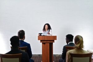 Public Speaking Certification - Confident woman delivering a speech to a diverse audience in a conference room.