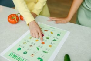 Diets Explained — Facts, Trends and Myths Certification - Close-up of hands pointing to a vegetable nutrition chart with fresh tomatoes on the table.