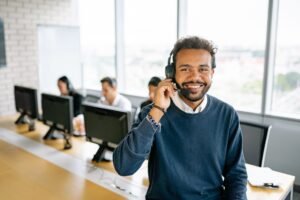 Achieving Sales on the Telephone Certification - Cheerful male call center agent with headset in a bright office environment.