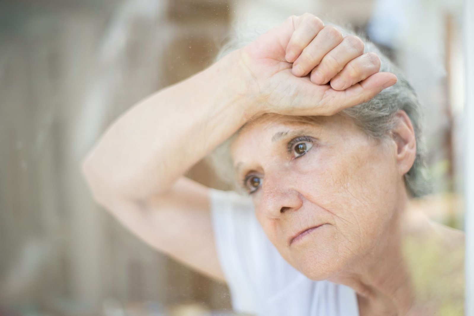 Dementia Awareness Certification - Thoughtful senior woman gazing through a window, symbolizing solitude and reflection.