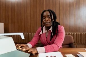 Legal Secretary Certification Level 3 - African American woman in a pink suit typing on a retro typewriter in an office setting.