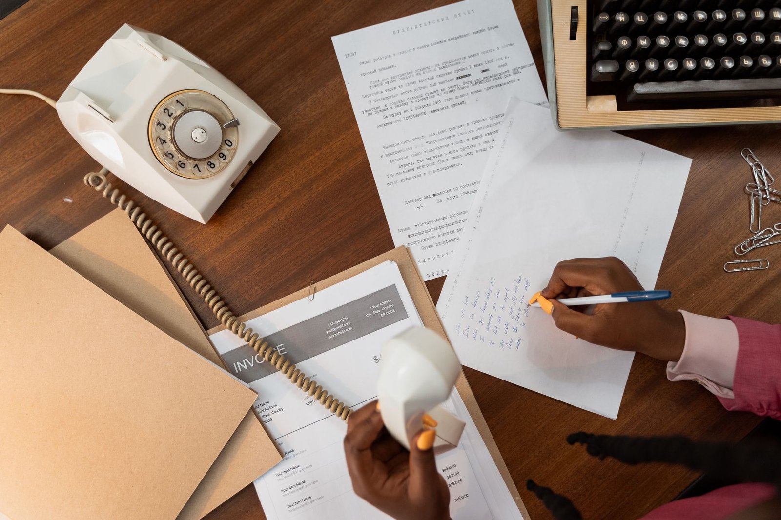Business Letter Writing Certification - Overhead view of a person writing notes while holding a vintage telephone on a wooden desk.
