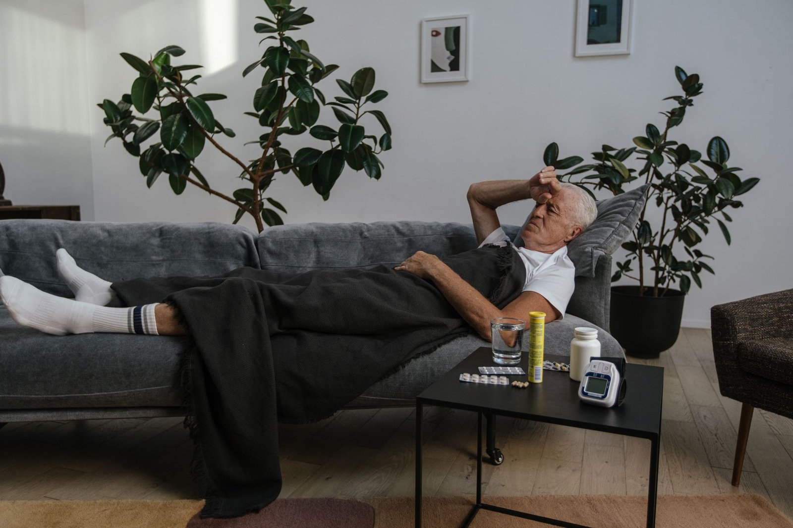 Sick Leave Certification - Senior man resting on a couch indoors with medicines on the table, looking unwell.