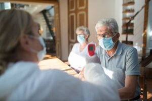 Safeguarding Adults at Risk Certification - Healthcare worker checks temperature of senior adults during pandemic using a thermometer in a home setting.