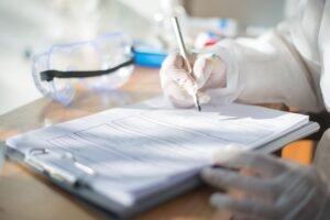 Method Statements Certification - Close-up of a scientist writing on a document with gloved hands in a laboratory setting.