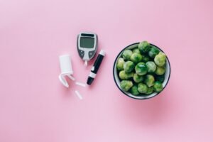 Nutrition for Diabetes Certification - Top view of a glucometer and fresh Brussels sprouts on a pink background promoting health.