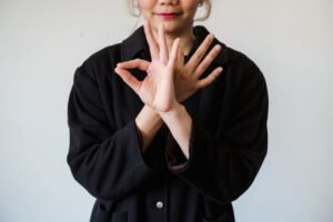 The Secrets of Body Language Certification - A person in a black jacket making unique hand gestures against a white background.