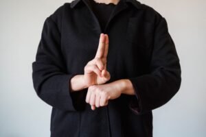 British Sign Language Certification - A person in a black coat demonstrating a sign language gesture indoors.