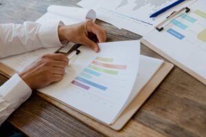 Evaluating a Marketing Plan Certification - Close-up of hands reviewing business report with colorful charts and graphs on a wooden desk.