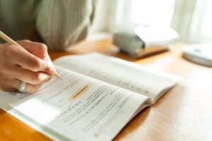 Introduction to Success Habits Certification - A student takes notes while studying at a sunlit desk with an open textbook.