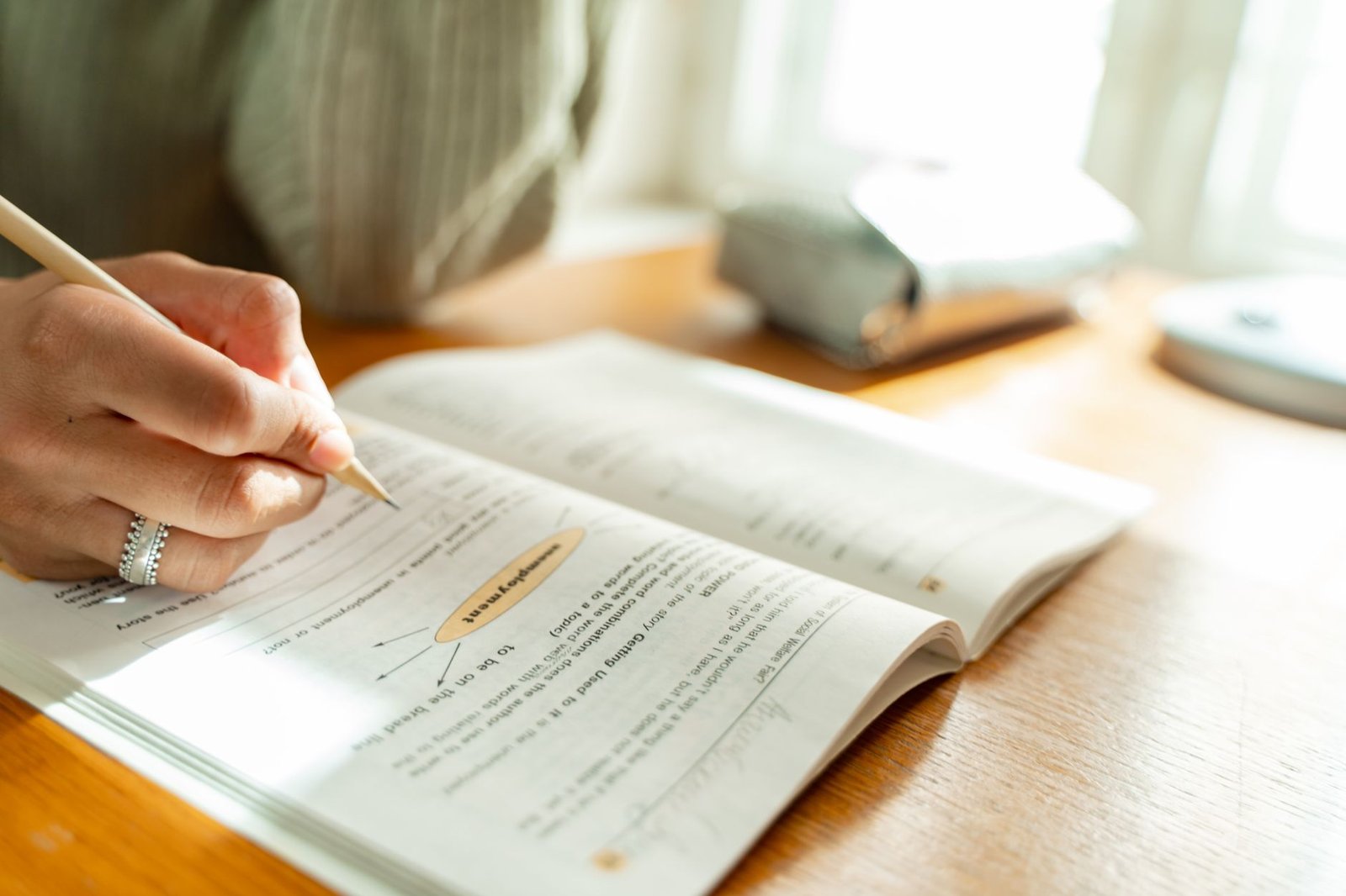 Introduction to Success Habits Certification - A student takes notes while studying at a sunlit desk with an open textbook.